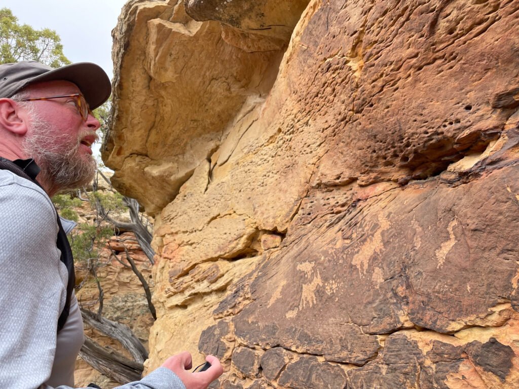 Radd Icenoggle looking closely at a petroglyph panel on a sandstone wall