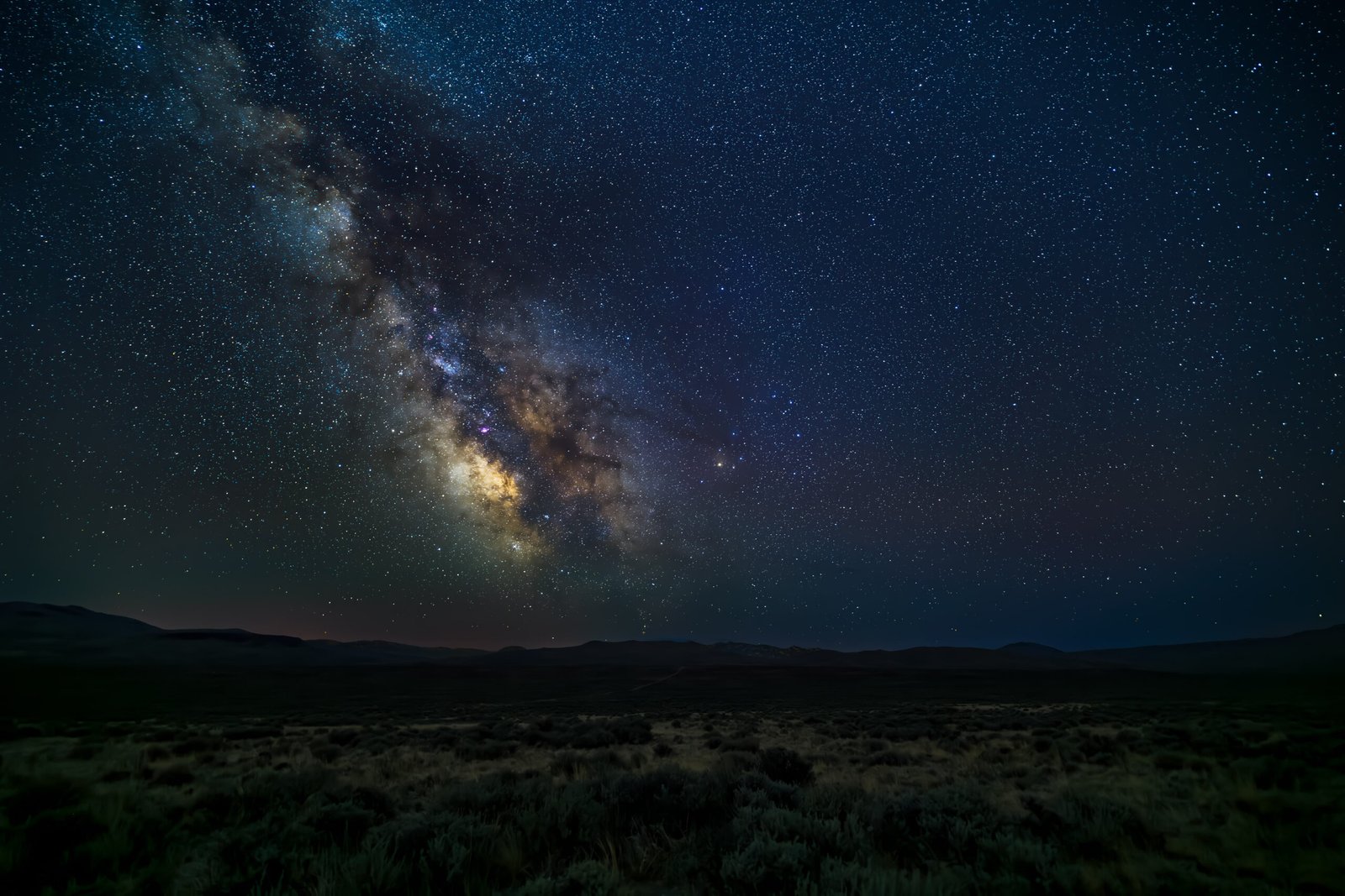 The Milky Way arching over a dark sagebrush horizon